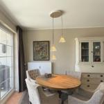 Esszimmer mit runden Tisch, vier Stühlen und weißen Schränken. An der Wand hängt ein Bild.