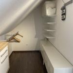 Dachbodenraum mit Schrank, Kleiderhaken und Regalen. Holzfußboden und schräges Dach.