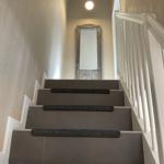 Treppenhaus mit grauer Treppe und weißem Geländer. Spiegel und Deckenleuchte sind sichtbar.