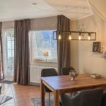 Esszimmer mit Holztisch, Stühlen und Fensterblick auf Wald.