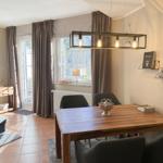 Esstisch mit Stühlen unter einer Lampe mit Hirschgeweih, vor Fenstern mit Vorhängen.