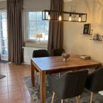 Esstisch mit vier Stühlen, Wandregale und Fenster mit Vorhängen.