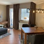 Ein Esszimmer mit Holztisch und Stühlen, daneben ein Wohnbereich mit Sofa und Fenster.