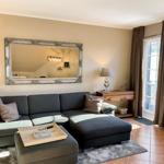 Ein Wohnzimmer mit grauem Sofa, Spiegel und Fenster mit Vorhängen.