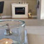 Brennende Teelichter in Glasbehälter vor Kamin und Schrank