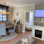 Wohn- und Essbereich mit Schlafzimmer im Hintergrund. Fernseher und Kamin im Vordergrund.