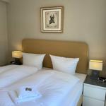 Doppelbett mit weißer Bettwäsche, zwei Nachttische mit Lampen und Bild an der Wand.