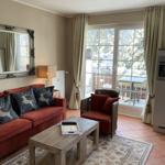 Wohnzimmer mit Sofa, Sessel und Terrasse. Durchgehende Glasfront mit Blick auf verschneite Bäume.