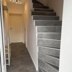 Haus mit Treppe und Flur mit weißen Türen und grauem Bodenbelag.