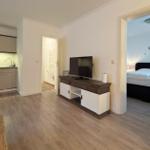 Wohnbereich mit Küche, TV und Blick in Schlafzimmer mit Bett und Wanddekoration.