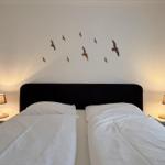 Zwei Betten mit weißen Laken, Nachttische mit Lampen und Vogel-Dekoration an der Wand.