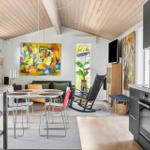 Kitchen with dining area and living room under wooden ceiling. Large wall art and plants.