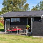 Black wooden house with terrace, table, benches, and grill area in the garden.