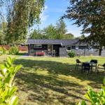 A dark holiday house with garden, terrace, and seating areas under trees.
