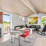 Living and dining area with table, chairs, sofa, and wall art. Wooden ceiling and large windows.