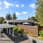 A modern house with terrace, wooden fence, and garden area under blue sky.