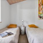 Two beds with yellow pillows, nightstand, and wall art. Window with view outside.