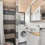 Bathroom with shower, washing machine, and sink. Wooden ceiling and window.