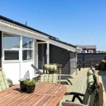 Deck with wooden table, chairs, and sun loungers. Background: house with windows and fence.