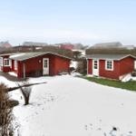 Zwei rote Holzhäuser mit weißen Fenstern und Türen stehen auf schneebedecktem Grundstück.