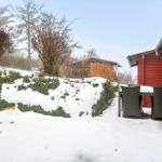 Roter Holzhaus mit Tisch und Stühlen im Schnee. Garten mit Sträuchern und Bäumen.