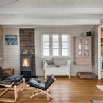 Wohnraum mit Kamin, Ledersessel und Fenstern. Küche und TV sichtbar.
