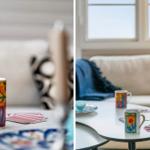 Tisch mit bunten Tassen und Karten vor einem Sofa mit blauem Decken.