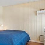 Schlafzimmer mit Bett, Schrank und Wandlampe. Holzwandverkleidung und Fenster.