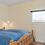Schlafzimmer mit Holzbett, blauer Bettdecke und Fenster mit Rollladen.