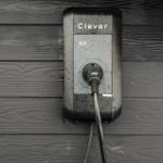 Außenliegender Elektroauto-Ladepunkt an dunkler Holzwand mit eingestecktem Kabel.