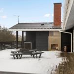 Terrasse mit Schnee, Sitzgelegenheiten und Holzdecke. Im Hintergrund steht ein kleines Gebäude mit Schornstein.