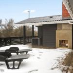Terrasse mit Schnee, Liegen und Außenkamin. Holzdecke und schwarze Holzwände.
