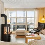 Wohnraum mit Kamin, Sofa, Sessel und großem Fenster. Holzfußboden und hell gestrichene Wände.