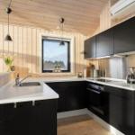 Kitchen with black cabinets, white countertops, and wood-paneled walls. Window with view of forest.