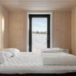 Bedroom with wooden walls and bed. Through door view of snowy landscape.