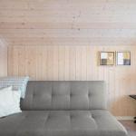 A gray sofa with cushions and a blanket in a room with wooden walls and two pictures.