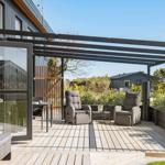 Terrasse mit Pavillon, zwei Sessel und Tisch. Holzdecke und Pflanzen umgeben den Außenbereich.