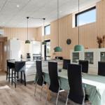 Moderne Küche mit Esstisch, schwarzen Stühlen und grünen Hängelampen an Holzwänden.