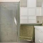 Badezimmer mit Dusche, Waschbecken und weißen Schränken an grünem Wandpaneel.