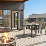 Terrasse mit Sitzgruppe, Esstisch und brennendem Feuerkorb. Hintergrund: Garten und Nachbarhaus.