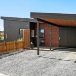 Moderne Hütte mit Holzverkleidung, überdachter Terrasse und Kiesplatz.