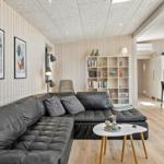 Wohnbereich mit Leder-Sofa, Bücherregal und Küchenbereich im Hintergrund.