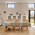 Esszimmer mit Holztisch, Stühlen und Glaswand. Küche und Terrasse sind sichtbar.