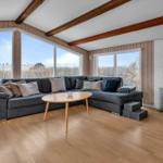Wohnzimmer mit Sofa, Kamin und großen Fenstern. Holzboden und Balken an der Decke.
