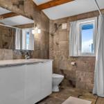 Badezimmer mit Dusche, Toilette und Waschbecken. Wände und Boden sind mit Steinplatten verkleidet.