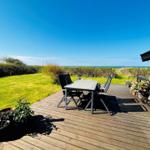 Terrasse mit Tisch und Stühlen, Blick auf Grünland und Meer, daneben Flagge und Pflanzen.