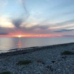 Sonnenuntergang über dem Meer mit Steinhügel im Vordergrund.