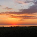 Sonnenuntergang über dem Meer mit Silhouetten von Menschen und einem Schiff im Hintergrund.