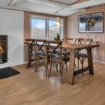 Esszimmer mit Holztisch, Stühlen und Kamin. Holzwände und Fenster mit Blick.