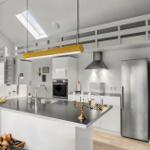 Modern kitchen with stainless steel appliances, dark countertop, and yellow pendant light under sloped ceilings.